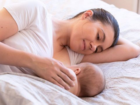 Beautiful mom lying at the back of the baby while the infant is sleeping on the white bed. Asian mother looking at the baby which is her child with love and care.