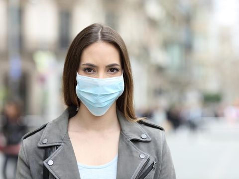 Front view portrait of serious woman with protective mask avoiding contagion looking at camera on street