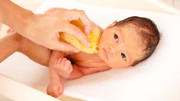 The mother cleaned the baby 2 months old, lying on the white cloth with the morning sun shining.