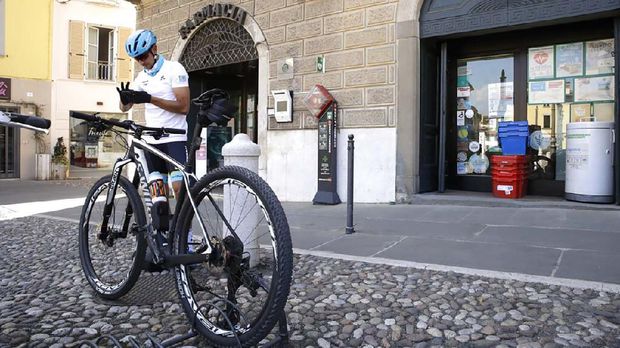 In this image taken on Tuesday, April 14, 2020, Italian professional cyclist Davide Martinelli, checks his smartphone to deliver medicine to residents in Rovato, near Brescia, Northern Italy. There are no fans lining the road. No teammates providing support. And no race to win. Professional cyclist Davide Martinelli has achieved a moral victory, though, by using his bike to help deliver medicine to elderly residents of his hometown in northern Italy during the coronavirus pandemic. (AP Photo/Luca Bruno)