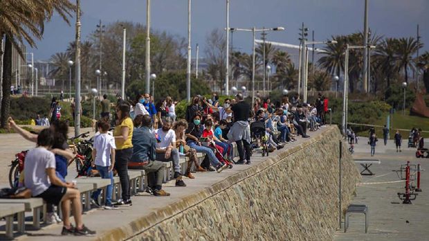 Families with their children sit in a boulevard as police patrol the beach, where access is prohibited, in Barcelona, Spain, Sunday, April 26, 2020 as the lockdown to combat the spread of coronavirus continues. On Sunday, children under 14 years old will be allowed to take walks with a parent for up to one hour and within one kilometer from home, ending six weeks of compete seclusion. (AP Photo/Emilio Morenatti)