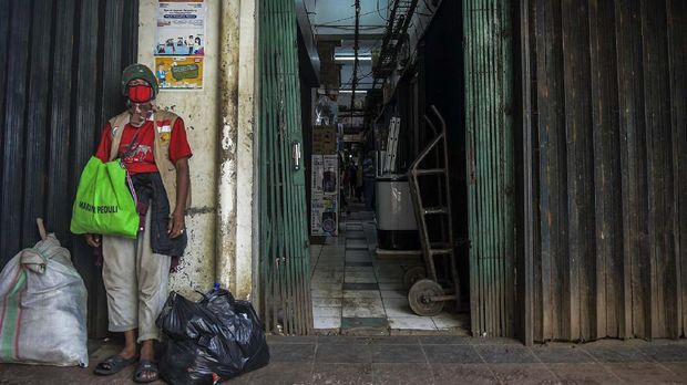 Seorang laki-laki mengenakan masker dan berdiri di depan toko yang tutup akibat merebaknya wabah COVID-19 di Pasar Minggu, Jakarta.