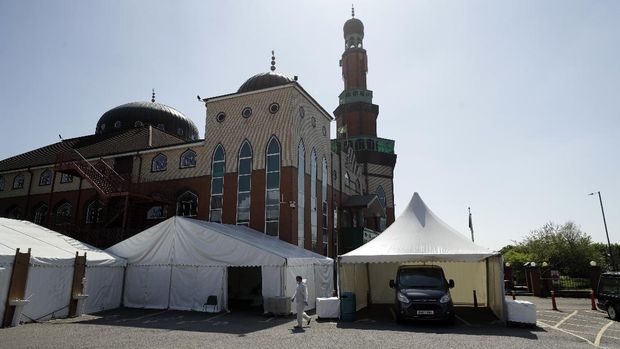 In this photo taken on Friday, April 24, 2020, a volunteer wearing protective clothing and a face mask to protect from coronavirus, walks through the car park of Central Jamia Mosque Ghamkol Sharif in Birmingham, England. The holy month of Ramadan is underway, and the Central Jamia Mosque Ghamkol Sharif should be full of worshippers. But this year, the main arrivals are the dead. While the mosque in the central England city of Birmingham has been closed in response to the coronavirus pandemic, its parking lot has been transformed into a temporary morgue with room for 150 bodies. (AP Photo/Matt Dunham)
