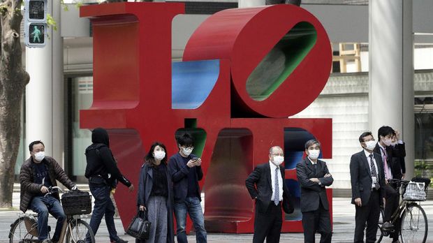 In this April 17, 2020, photo, pedestrians wait for crossing street in front of a statue at Shinjuku business district in Tokyo. Under Japan's coronavirus state of emergency, people have been asked to stay home. Many are not. Some still have to commute to their jobs despite risks of infection, while others are dining out, picnicking in parks and crowding into grocery stores with scant regard for social distancing. (AP Photo/Eugene Hoshiko)