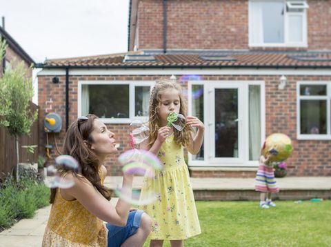 A mother and daughter are playing together in the backyard.  The are blowing bubbles.