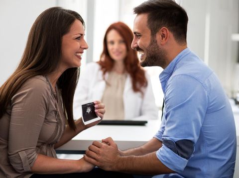 Mother holding ultrasound, husband and wife in a clinic, beautiful family.
