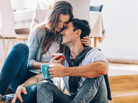 Happy couple in love sitting on the floor, embracing, smiling and drinking coffee, with copy space.