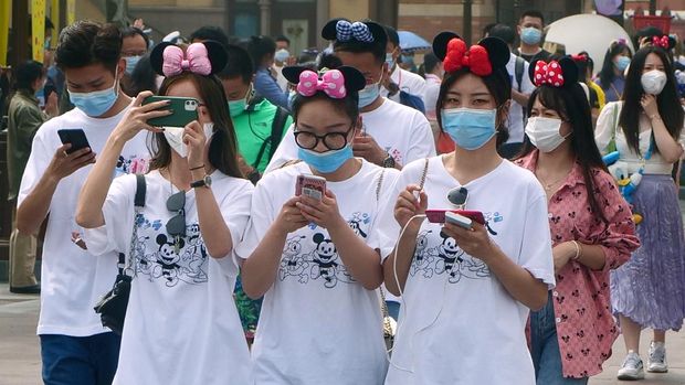 Visitors, wearing face masks, enter the Disneyland theme park in Shanghai as it reopened, Monday, May 11, 2020. Visits will be limited initially and must be booked in advance, and the company said it will increase cleaning and require social distancing in lines for the various attractions.(AP Photo/Sam McNeil)