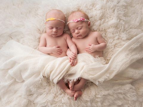 Seven week old fraternal, twin baby girls sleeping on a white flokati rug.