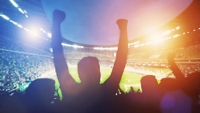 Happy football fans support their team and celebrating goal with hands up. Big stadium