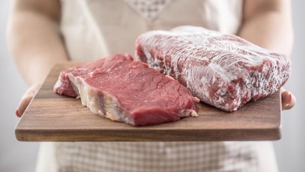 Female cook holding wooden board of raw and frozen beef  meat.