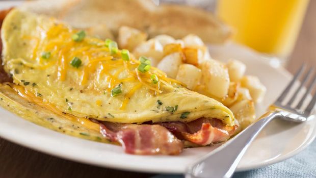 A macro photograph of a bacon cheddar omelet with home fries (potatoes), orange juice, and toast.  The breakfast place setting  is set on a rustic wood table with a blue napkin.  Please see my portfolio for other food and drink images.