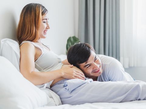 Young Asian husband touching/listening on belly pregnant wife with love and happy