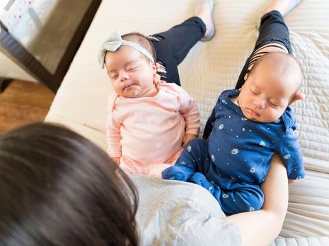 High angle view of mother holding adorable twin kids on bed
