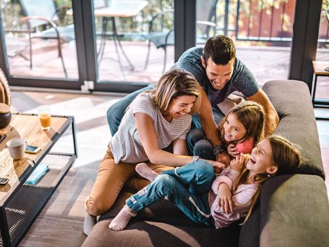 High angle view of cheerful parents having fun while tickling their daughters on sofa in the living room.