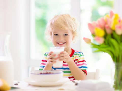 Child having breakfast. Kid drinking milk and eating cereal with fruit. Little boy at white dining table in kitchen at window. Kids eat on sunny morning. Healthy balanced nutrition for young kids.