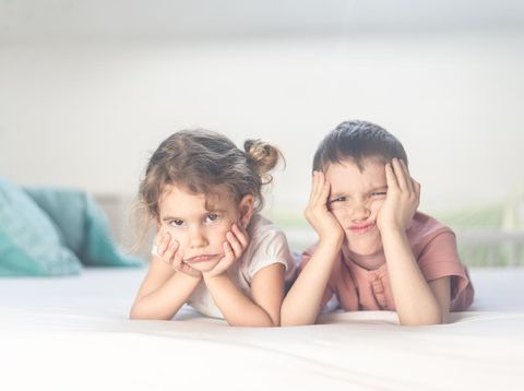 Beautiful brother and sister are lying down in bedroom and having so much fun smiling and making silly faces.
