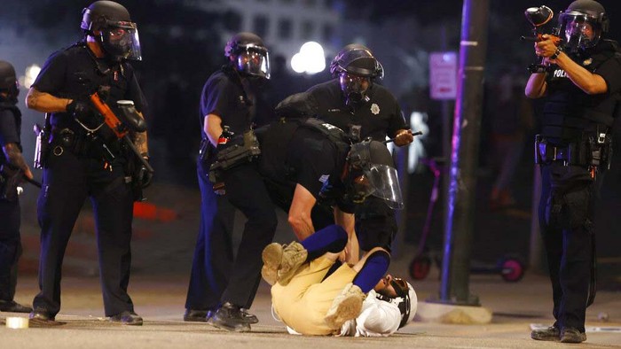 Denver Police Department officers stand over a man who fell to the street after they used tear gas and rubber bullets to disperse a protest outside the State Capitol over the death of George Floyd, a handcuffed black man who died in police custody in Minneapolis, late Thursday, May 28, 2020, in Denver. (AP Photo/David Zalubowski)