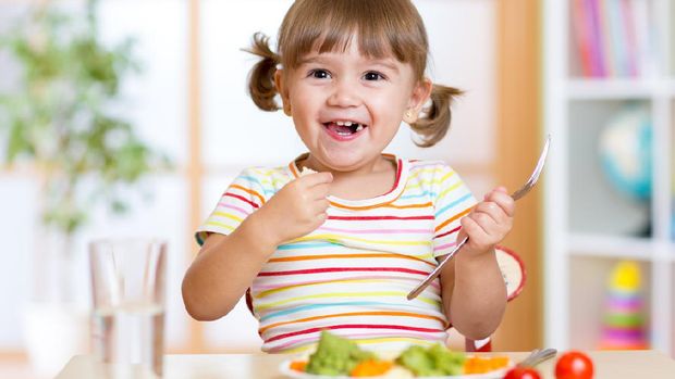 smiling kid girl eating healthy vegetables at kitchen