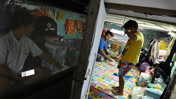 This photo taken on May 28, 2020 shows Papassorn Sroirvengsri speaking to her son Kittipat as her husband Thanapat Noidee looks on in their home in Bangkok. - Shuffling around their tiny slum home which is too small to stand up in, a couple share donated noodles with their sons and worry about how they will pay the bills, as the coronavirus pushes Thailand's poor deeper into penury. (Photo by Romeo GACAD / AFP) / TO GO WITH Health-virus-Thailand-economy-poverty by Pitcha DANGPRASITH