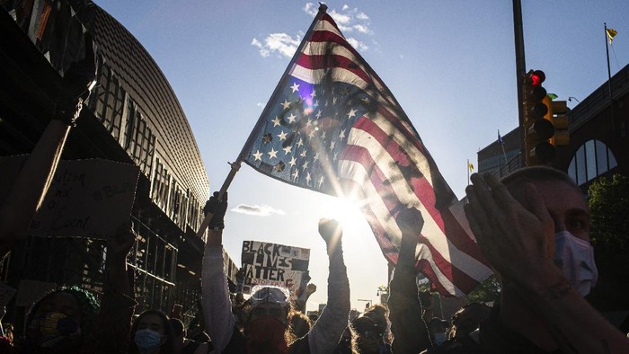 A man holds a U.S. flag upside down, a sign of distress, as protesters march down the street during a solidarity rally for George Floyd, Sunday, May 31, 2020, in the Brooklyn borough of New York. Protests were held throughout the city over the death of Floyd, a black man in police custody in Minneapolis who died after being restrained by police officers on Memorial Day. (AP Photo/Wong Maye-E)