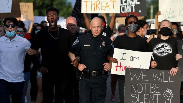 Cinta dan Respek di Tengah Aksi Antirasisme George Floyd O'Fallon (Mo.) police Chief Tim Clothier, center, walks arm-in-arm with Ryan Staples, left, and Jalen Thompson, right, at the front of a march for George Floyd in O