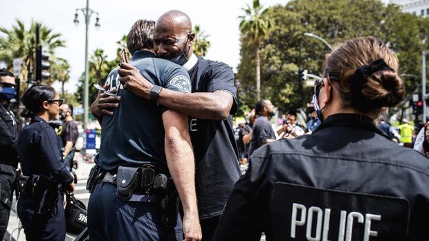 Pastor Calvin Sparks, of Life Pavilion in Carson, hugs LAPD officers after some officers took a knee with clergy and marchers at LAPD Headquarters during a demonstration demanding justice for George Floyd, Tuesday, June 2, 2020 in Los Angeles, Floyd, a black man, died after being restrained by Minneapolis police officers on May 25.  (Sarah Reingewirtz/The Orange County Register via AP)