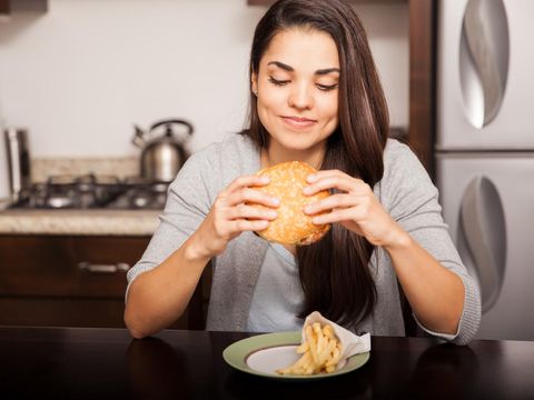 Beautiful young brunette about to bite a delicious hamburger at home