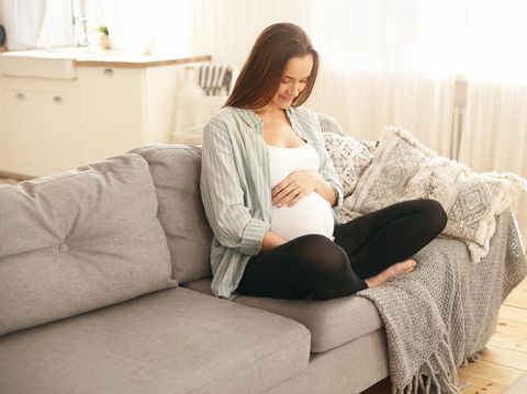 Curious little daughter touching her pregnant mother big tummy, home interior