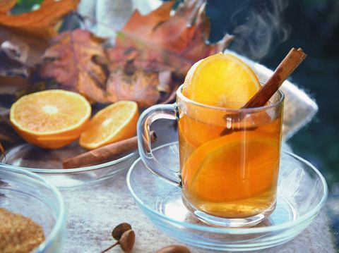 hot ginger tea with orange slices and cinnamon in a glass cup on a blanket and some red autumn leaves, selected focus, narrow depth of field