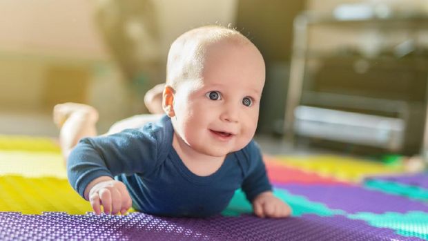 Portrait of cute caucasian baby boy crawling on soft playing mat indoors. Adorable child having fun making making first steps on floor at nursery. Backlit.  Happy childhood and evolution concept.