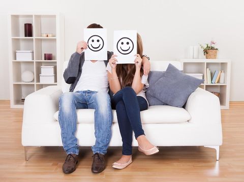Couple covered faces with smiley white paper.