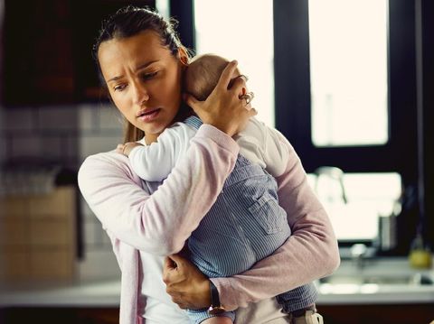 Young mother holding her baby son and consoling him at home.