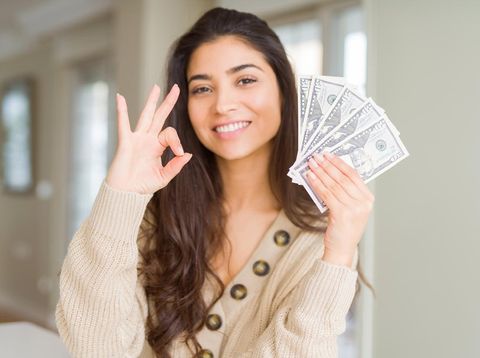 Young woman holding 50 dollars bank notes doing ok sign with fingers, excellent symbol