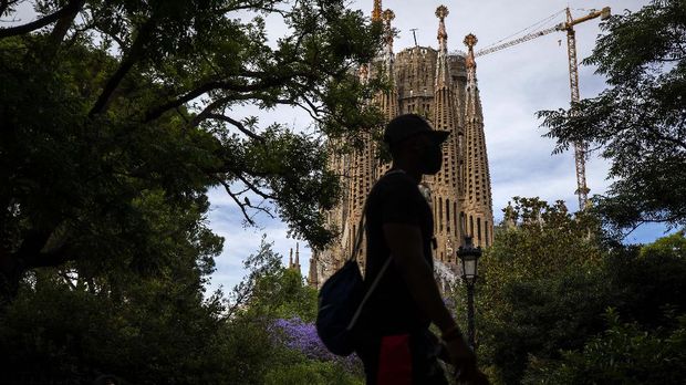 In this Sunday, May 31, 2020 photo, local visitors walk in a park next to the Antoni Gaudí's La Sagrada Familia Basilica in Barcelona. Tourism is a pillar of Spain's economy. Eighty million annual visitors generate 12% of Spain's GDP and help employ 2.6 million people. (AP Photo/Emilio Morenatti)