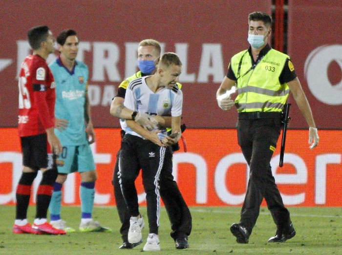 A supporter invades the pitch with FC Barcelonas Lionel Messi behind left during the Spanish La Liga soccer match between Mallorca and FC Barcelona at Son Moix Stadium in Palma de Mallorca, Spain, Saturday, June 13, 2020. With virtual crowds, daily matches and lots of testing for the coronavirus, soccer is coming back to Spain. The Spanish league resumes this week more than three months after it was suspended because of the COVID-19 pandemic. (AP Photo/Francisco Ubilla)