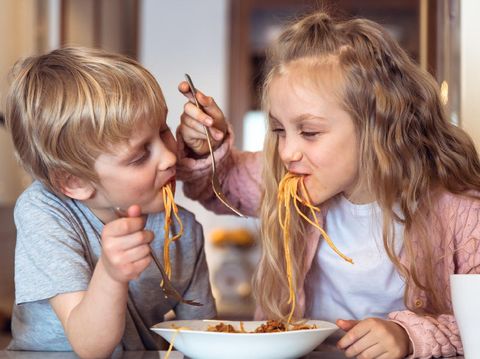 Cute children having fun while eating spaghetti with bolognese sauce at home