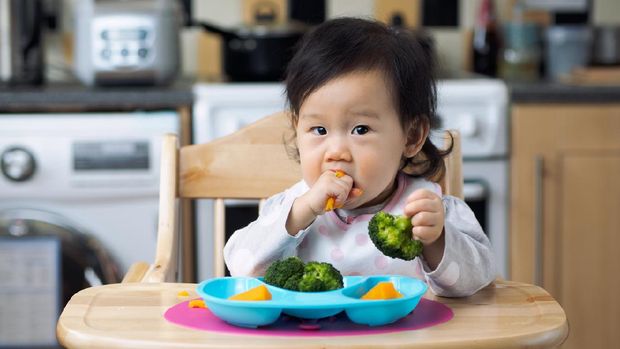 Asian baby girl eating vegetable first time at home kitchen