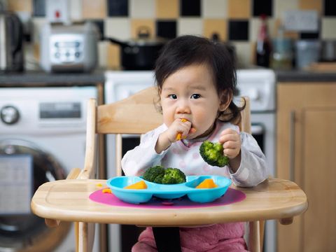 Asian baby girl eating vegetable first time at home kitchen