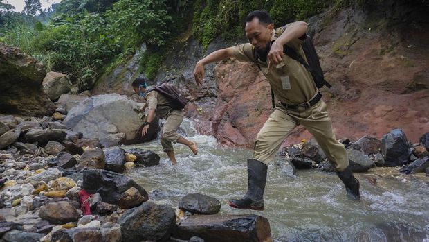 Kepala Sekolah SMP N 4 Bawang Mulud Sugito (kanan) dan guru Wiyata Bhakti melewati aliran sungai di dasar bukit saat mengantar lembar tugas siswa secara langsung ke rumahnya di Pranten, Kecamatan Bawang, Kabupaten Batang, Jawa Tengah.