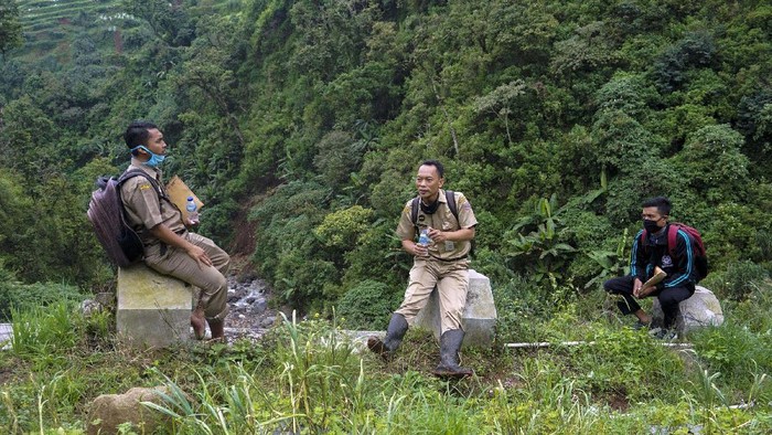 Kepala Sekolah SMP N 4 Bawang Mulud Sugito (tengah) dan guru Wiyata Bhakti bersiap melewati aliran sungai di dasar bukit saat mengantar lembar tugas siswa secara langsung ke rumahnya di Pranten, Kecamatan Bawang, Kabupaten Batang, Jawa Tengah.