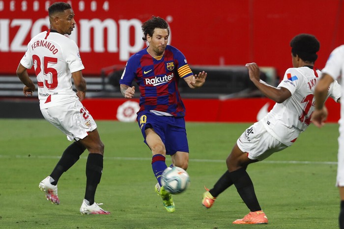 Barcelonas Lionel Messi, center, vies for the ball with Sevillas Jules Kounde, right, during the Spanish La Liga soccer match between Sevilla and FC Barcelona at the Ramon Sanchez-Pizjuan stadium in Seville, Spain, Friday, June 19, 2020. (AP Photo/Angel Fernandez)