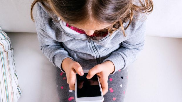 Little girl sitting on sofa with a smart phone. Happy child playing indoors.