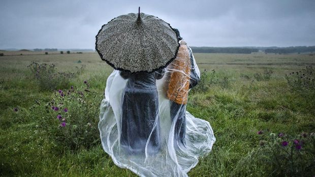 People shield from the rain next to the closed Stonehenge as people gather to celebrate the Summer Solstice, the longest day of the year, near Salisbury, England, Sunday June 21, 2020. (Ben Birchall/PA via AP)