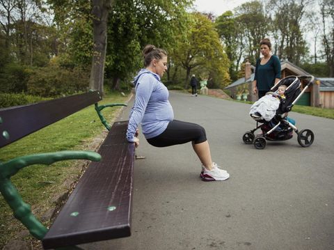 A pregnant fitness instructor is demonstrating how to do a reverse push up to one of the mothers in her fitness bootcamp.