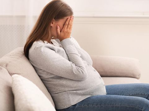 Depression And Pregnancy. Pregnant Lady Crying Covering Face With Hands Sitting On Sofa At Home.