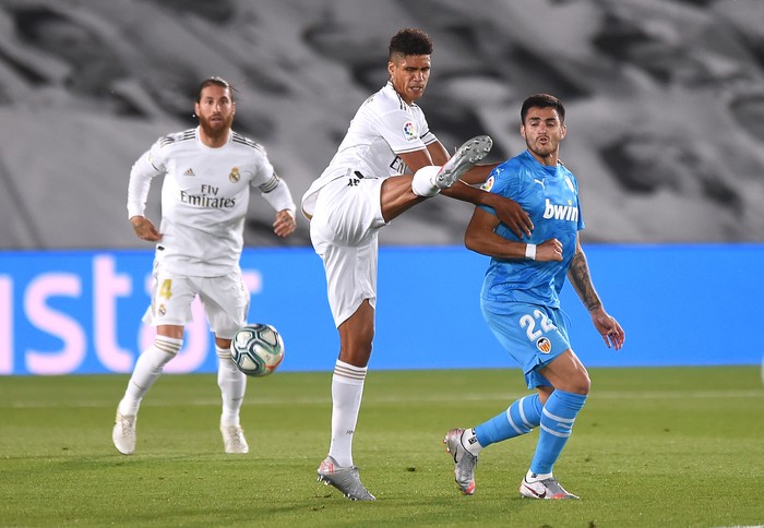 MADRID, SPAIN - JUNE 18:  Raphaël Varane of Real Madrid CF is fouled by Maximiliano Gómez of Valencia CF during the Liga match between Real Madrid CF and Valencia CF at Estadio Alfredo Di Stefano on June 18, 2020 in Madrid, Spain. (Photo by Denis Doyle/Getty Images)