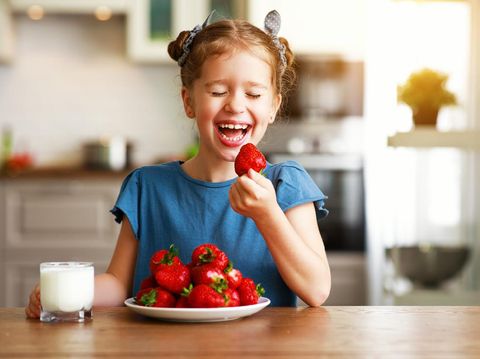 happy child girl eating strawberries with milk at home