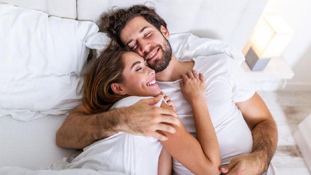 Beautiful loving couple kissing in bed. beautiful young couple lying together on the bed. Romantic young couple in love lying on bed. Beautiful couple smiling in bed.