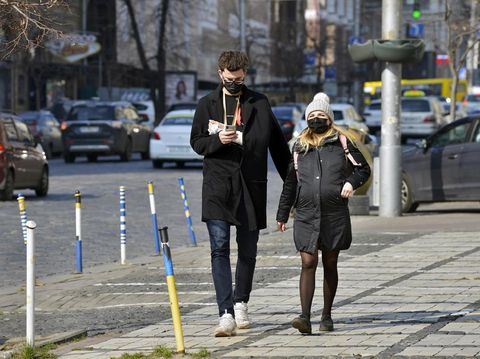 Kyiv, Ukraine - March 18, 2020: Pregnant woman and man with plaster on hand in protective medical mask walking down the street. Due to the coronavirus epidemic, the Ukrainian government has closed the subway.
